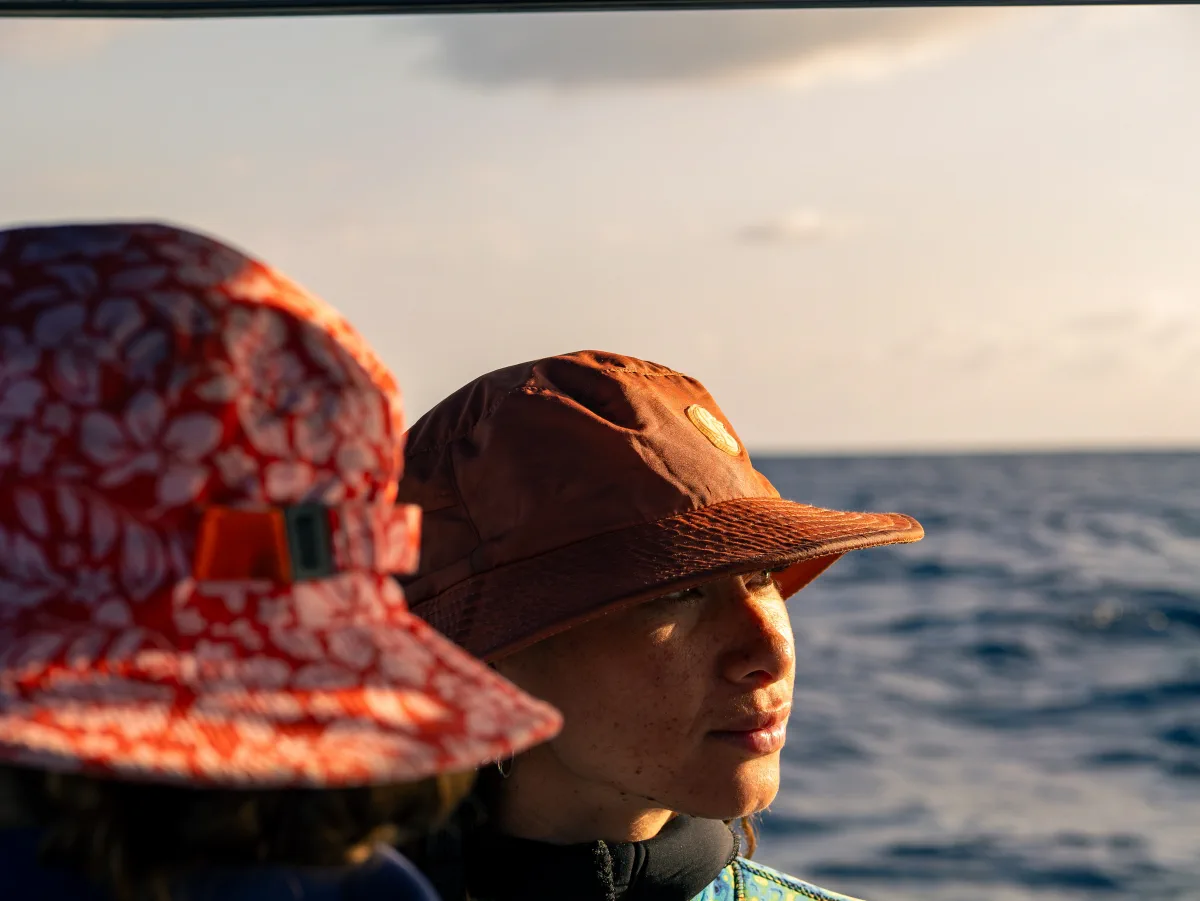 Two women in sun hats looking out across the ocean in warm evening light