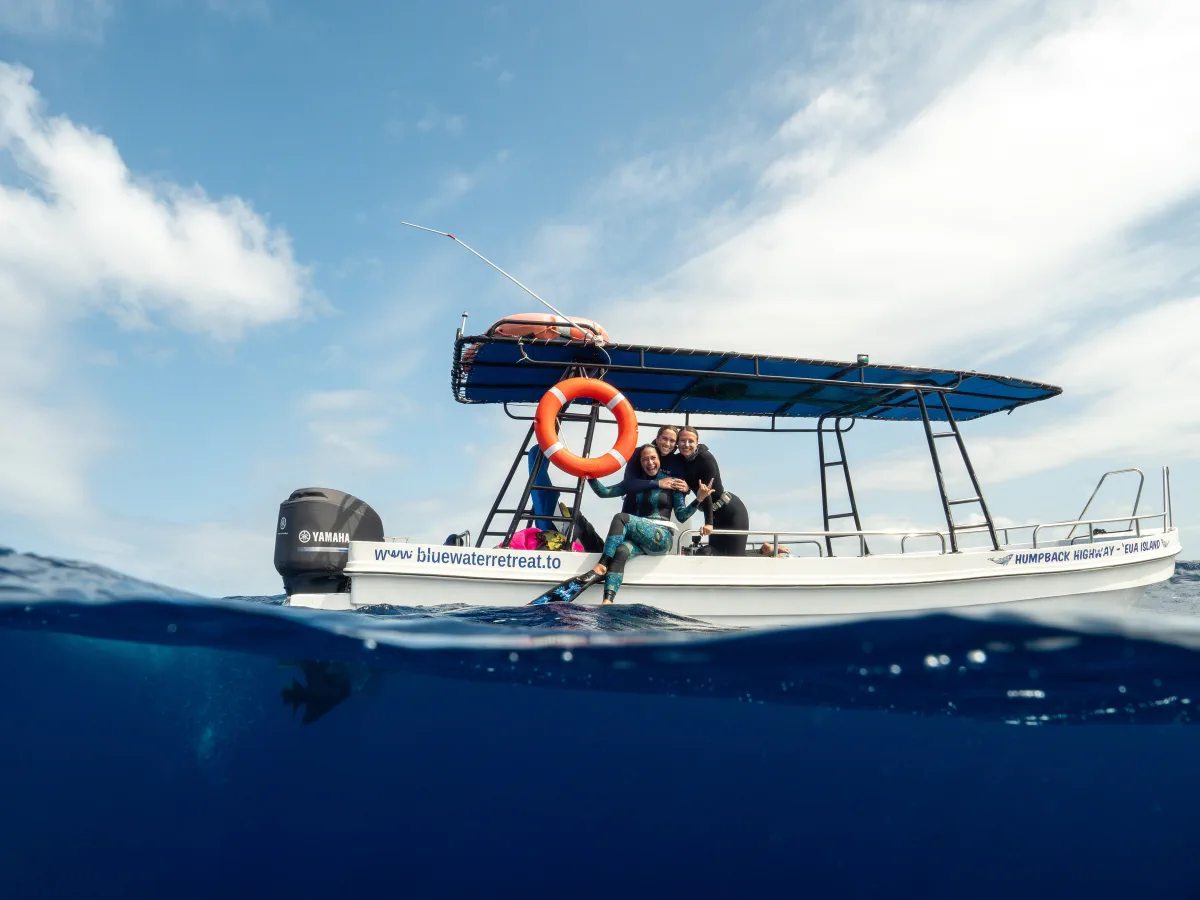 A small expedition boat seen at water level beneath a bright blue sky in Tonga