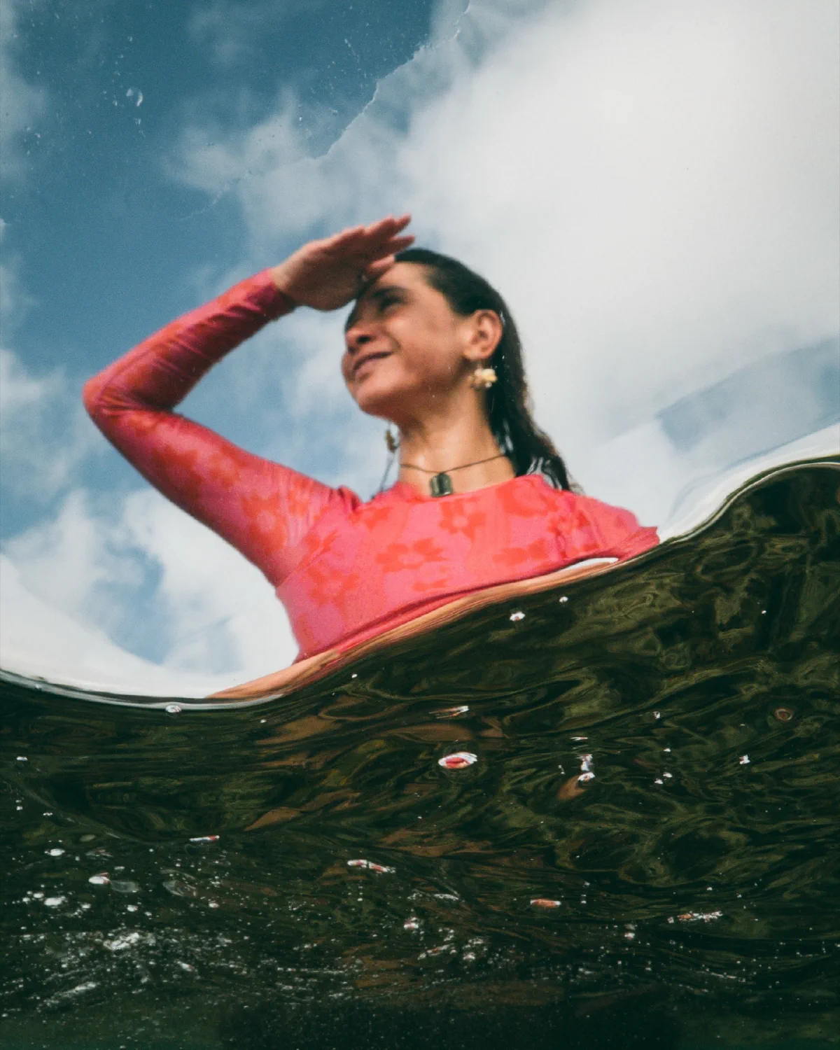 Hannah in a red rashie at the waterline beneath a bright sky