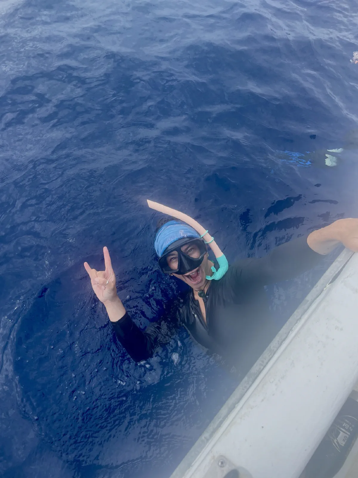 Tee smiling beside the boat and making a rock-on hand sign